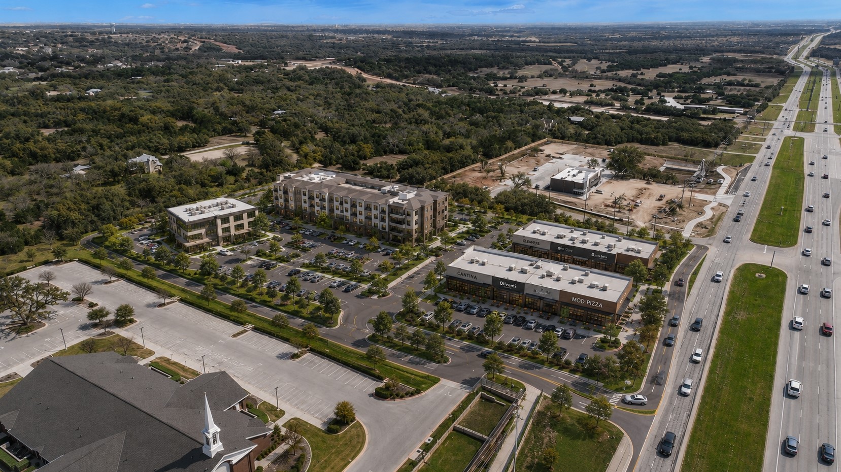 51 County Road 264 Leander, TX 78641 - Photo 6 of 17 An aerial perspective reveals a vibrant mixed-use development alongside a major thoroughfare, surrounded by verdant landscapes.