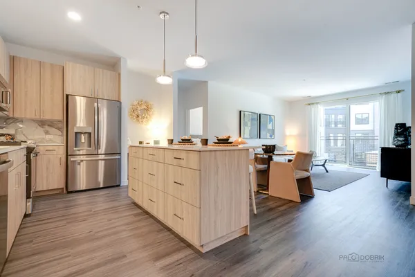 a kitchen with kitchen island granite countertop a refrigerator a stove a dining table and chairs with wooden floor