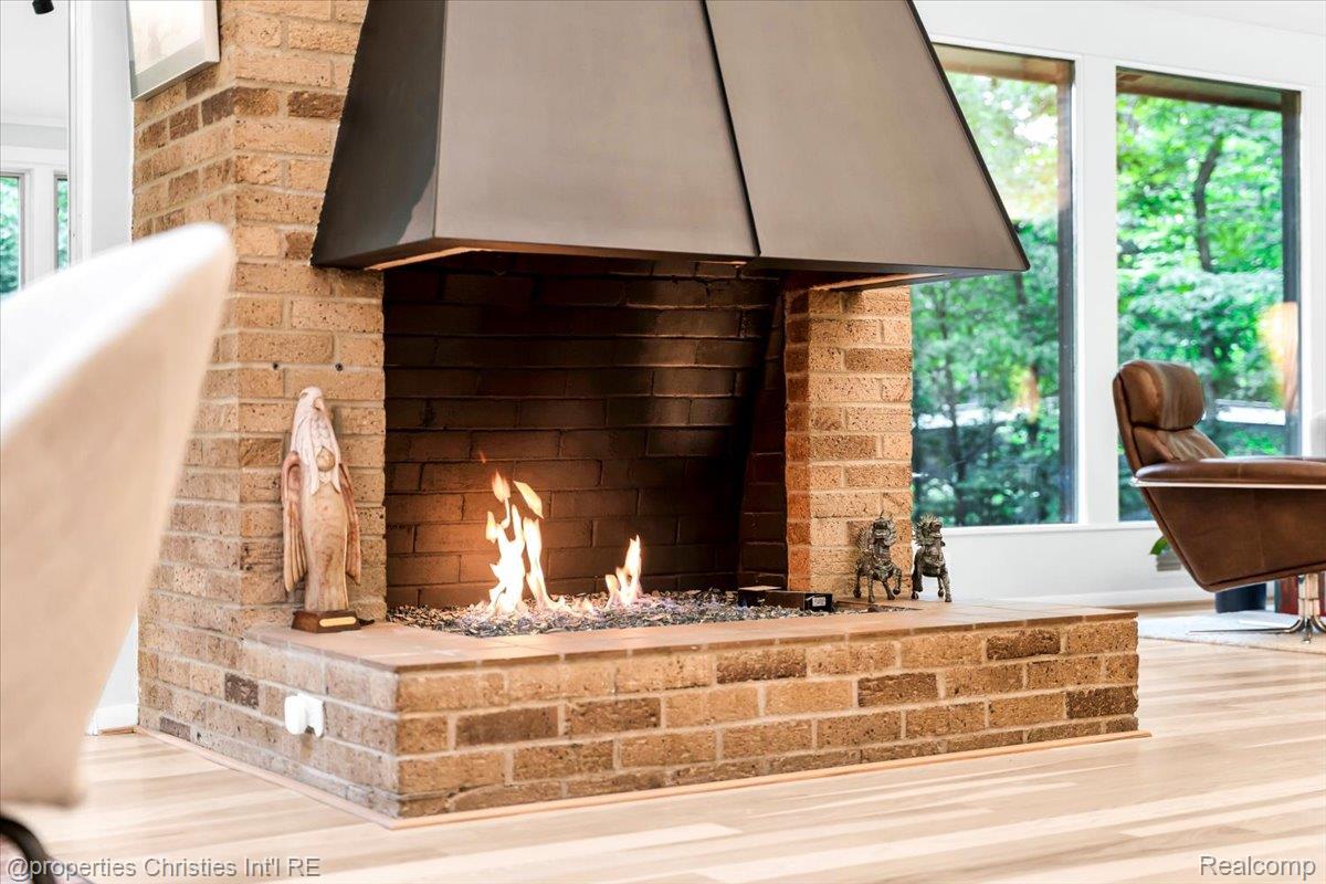 3939 Charing Cross Road Bloomfield Hills, MI 48304 - Photo 16 of 33 Brick fireplace with a dark metal hood, featuring a glass firebed, and light wood-finish flooring