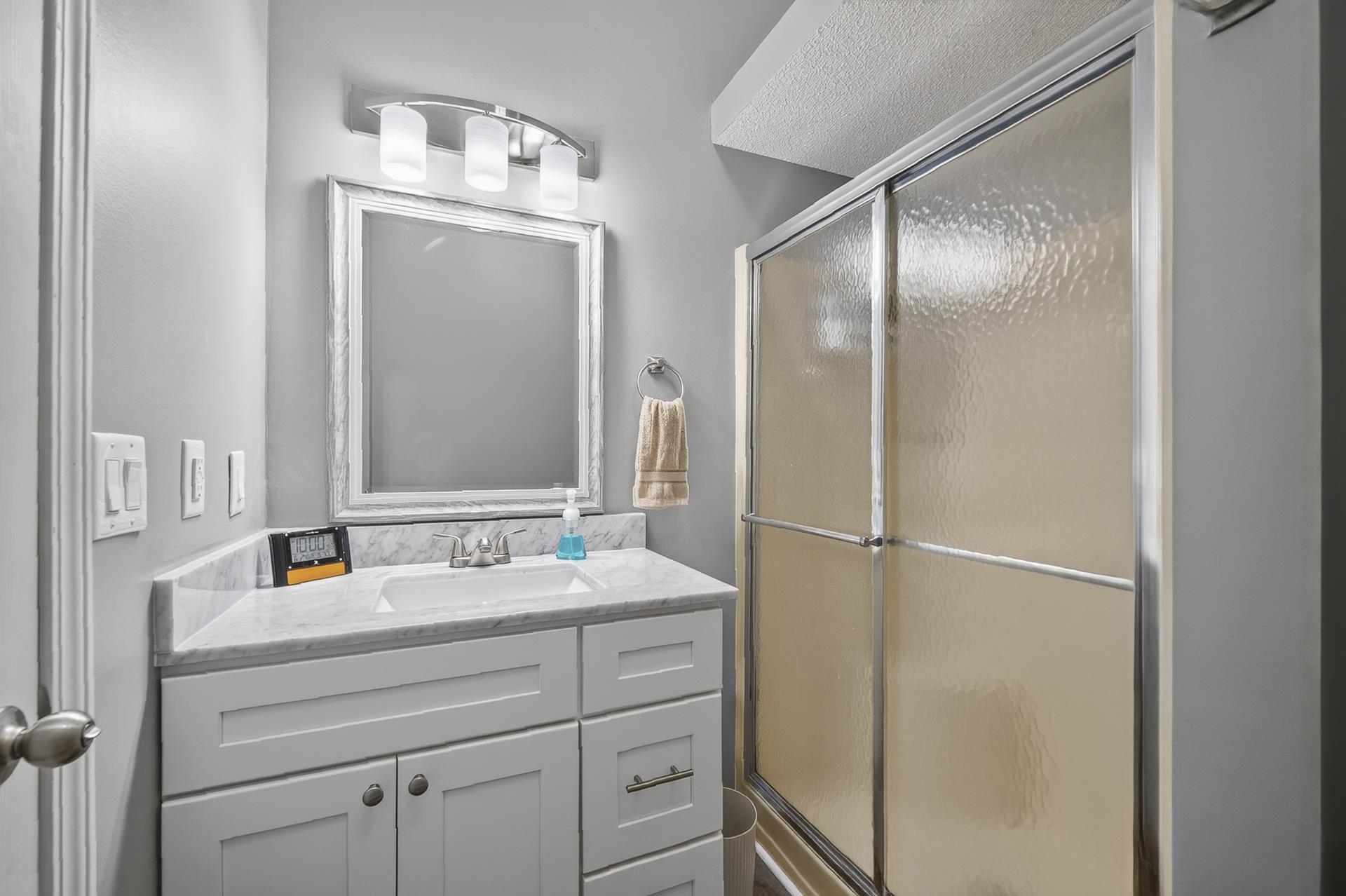 74 Driftwood Road Counce, TN 38326 - Photo 35 of 40 Bathroom featuring a single vanity with a white countertop and undermount sink, white shaker-style cabinetry, a framed mirror, and a shower with sliding textured glass doors
