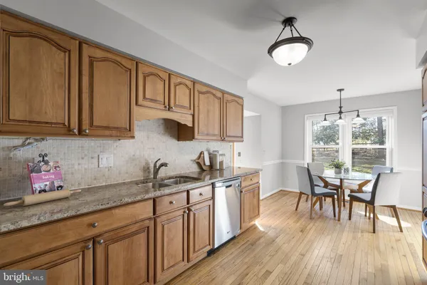 a kitchen with stainless steel appliances granite countertop a sink dishwasher cabinets a dining table and chairs with wooden floor