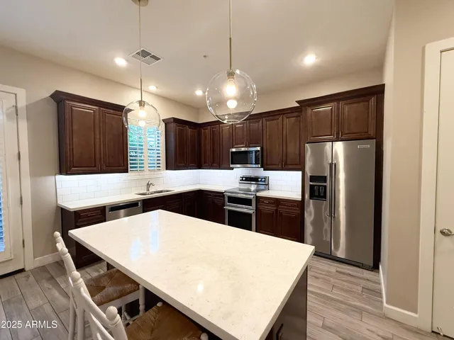 a kitchen with stainless steel appliances kitchen island a table chairs sink and refrigerator