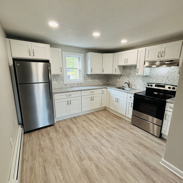 16 A Exeter Street Lawrence, MA 01843 - Photo 3 of 12 a kitchen with wooden floors white cabinets and stainless steel appliances