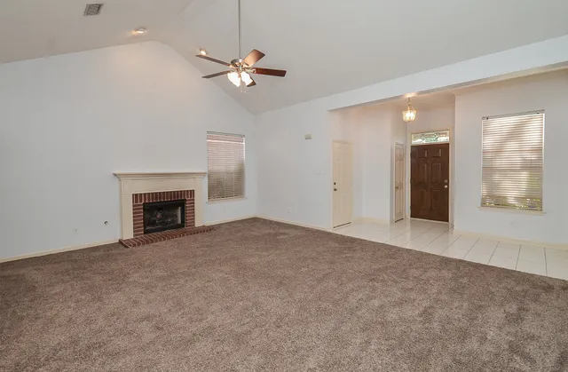 a view of an empty room with chandelier fan and fire place