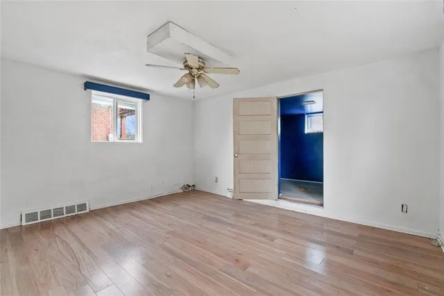 a view of an empty room with wooden floor and a ceiling fan