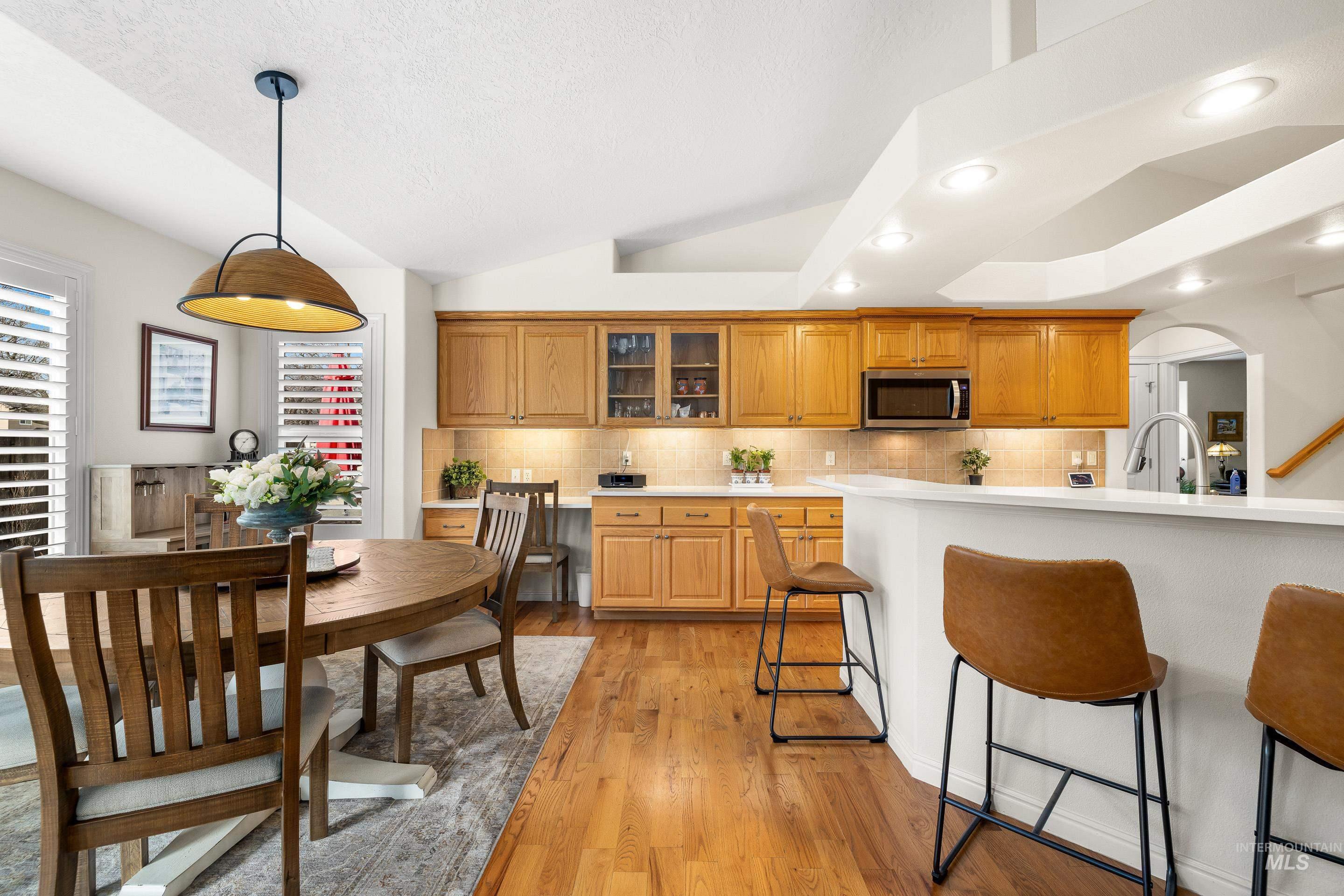3631 North Alexis Way Meridian, ID 83646 - Photo 15 of 49 Kitchen with arched walkways, lofted ceiling, hanging light fixtures, glass insert cabinets, and light wood finished floors