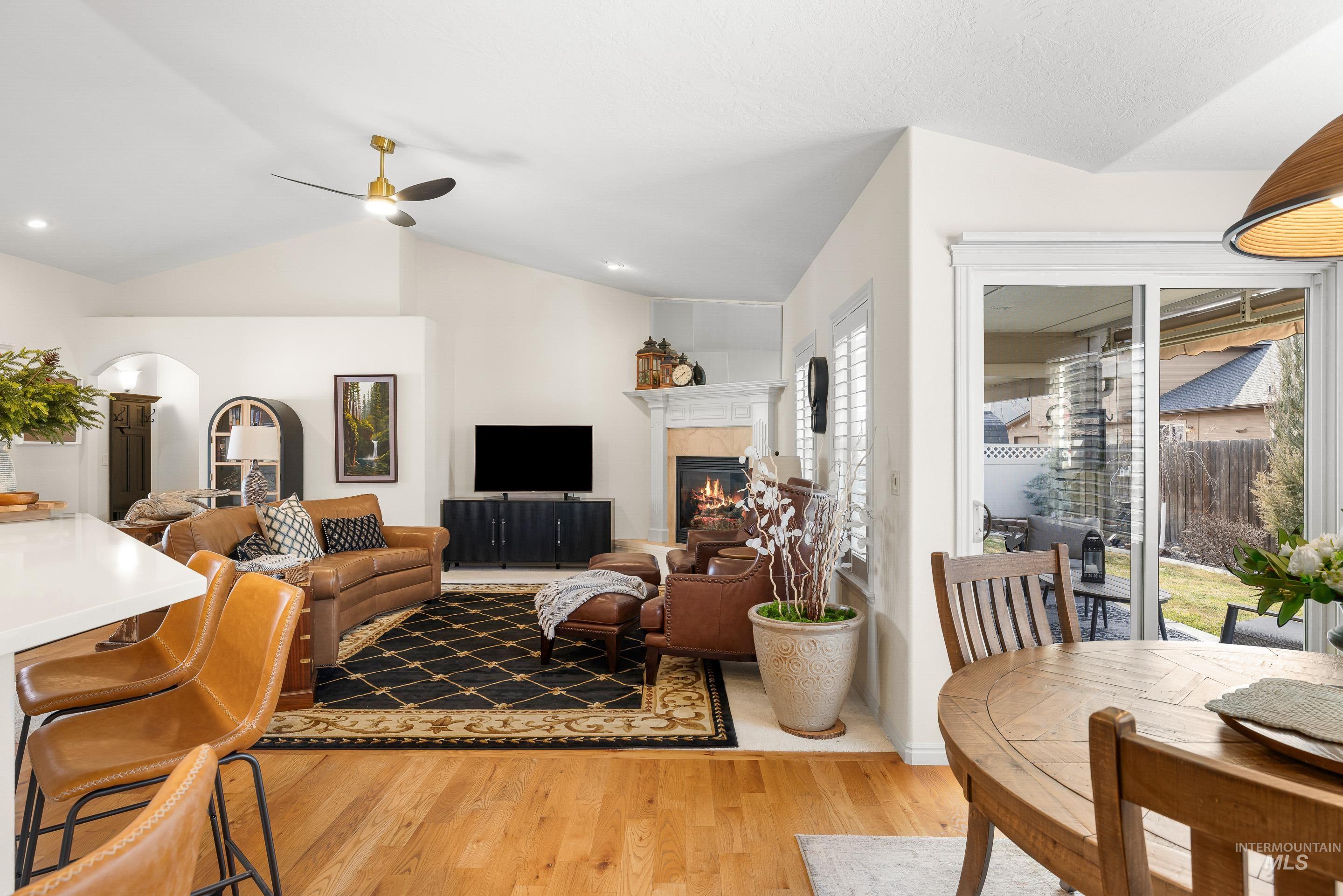 3631 North Alexis Way Meridian, ID 83646 - Photo 17 of 49 Living room with a tiled fireplace, light wood finished floors, arched walkways, vaulted ceiling, and ceiling fan