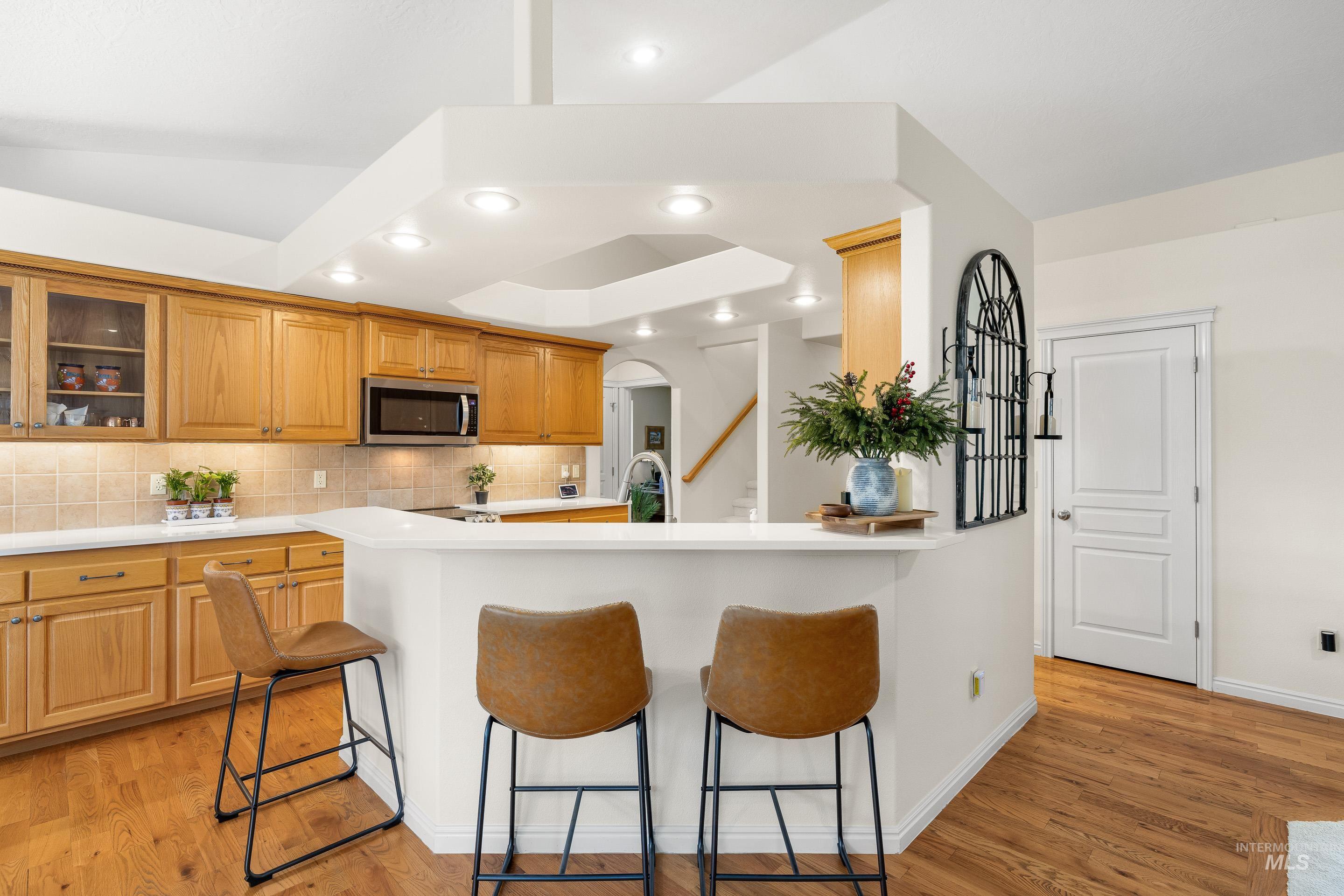 3631 North Alexis Way Meridian, ID 83646 - Photo 18 of 49 Kitchen featuring a kitchen bar, arched walkways, glass insert cabinets, light wood-type flooring, and stainless steel microwave