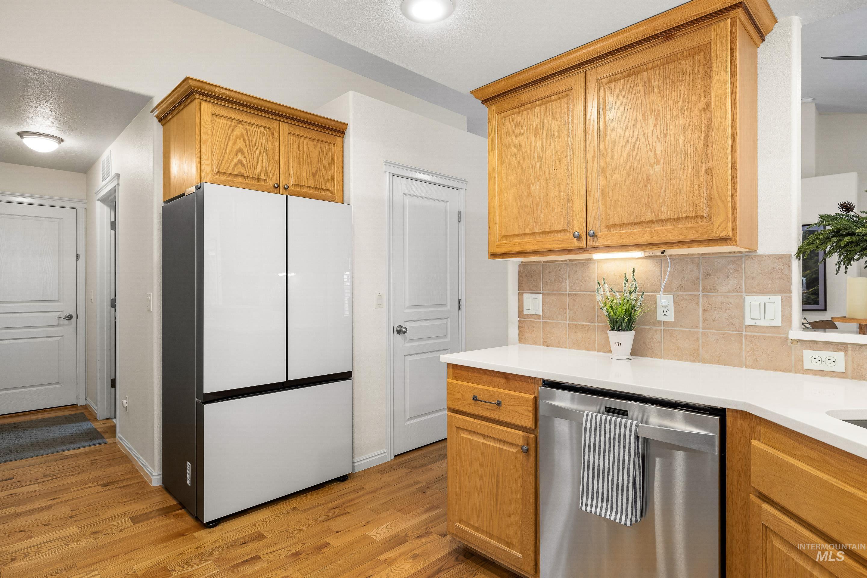 3631 North Alexis Way Meridian, ID 83646 - Photo 20 of 49 Kitchen with freestanding refrigerator, dishwasher, decorative backsplash, light wood-style floors, and light stone countertops