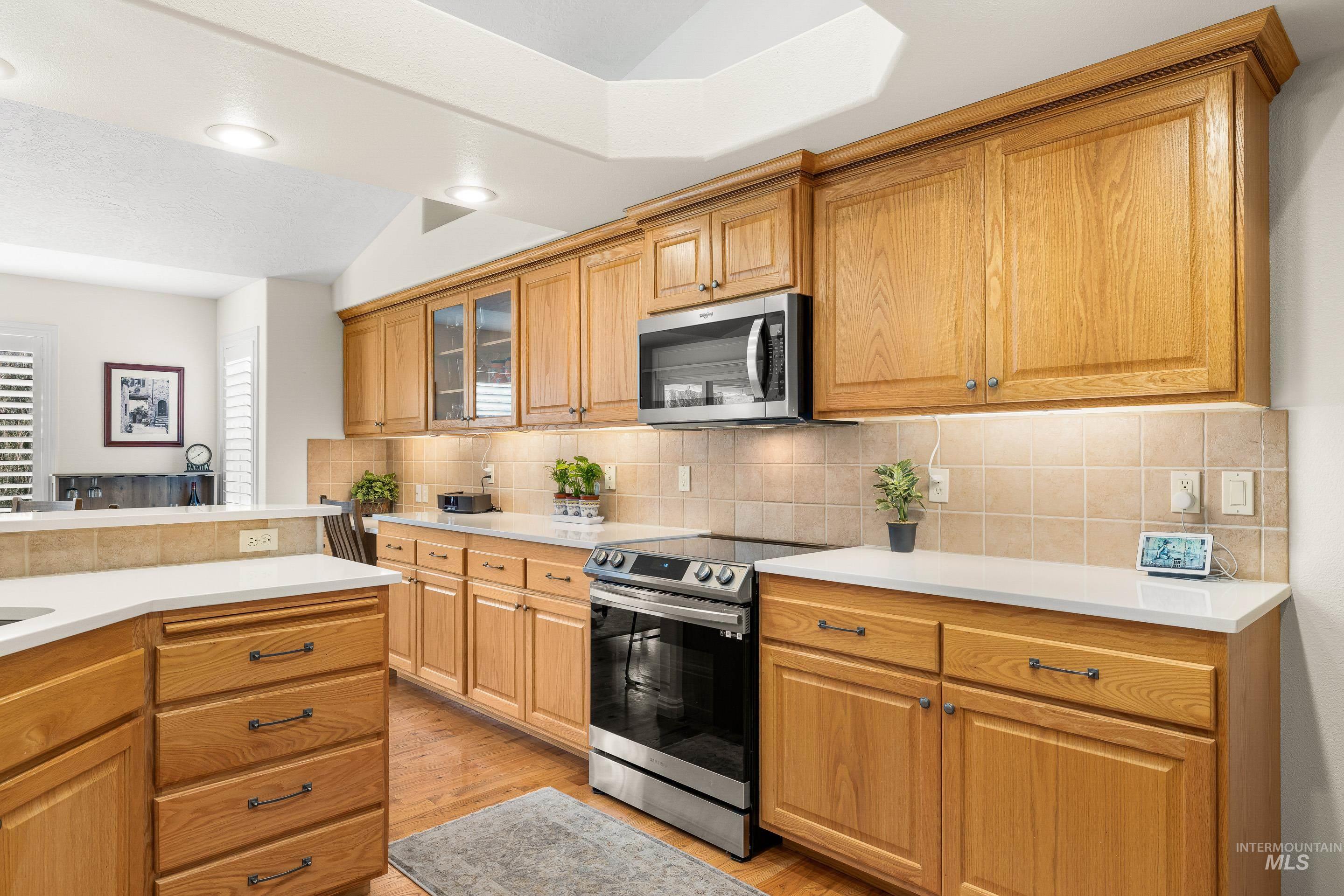 3631 North Alexis Way Meridian, ID 83646 - Photo 24 of 49 Kitchen with appliances with stainless steel finishes, light wood-type flooring, tasteful backsplash, glass insert cabinets, and lofted ceiling