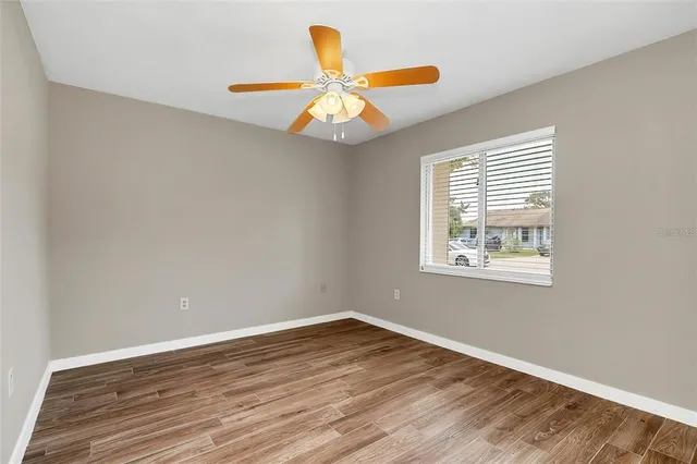 an empty room with wooden floor fan and windows