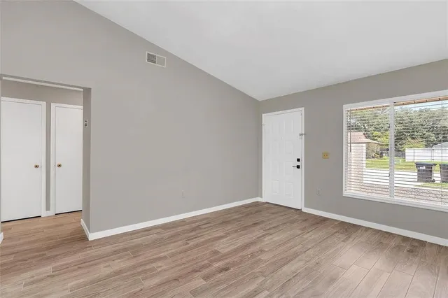 a view of an empty room with wooden floor and a window
