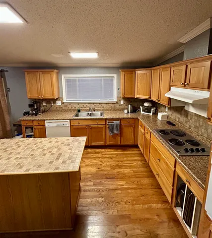 a large kitchen with stainless steel appliances granite countertop a stove top oven a sink dishwasher a dining table and chairs with wooden floor