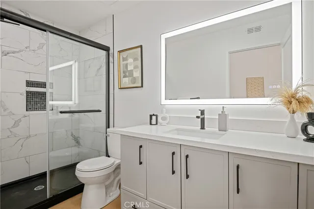 a bathroom with a granite countertop sink a toilet a mirror and shower