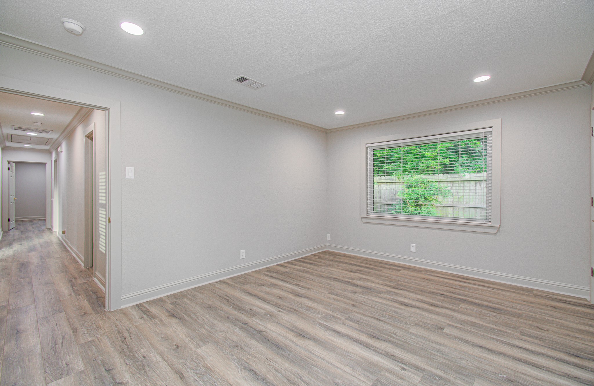 1801 Benbow Way Houston, TX 77080 - Photo 26 of 32 This room features light hardwood floors, neutral walls, and recessed lighting. A large window offers natural light and views of greenery. The adjoining hallway leads to other areas of the home, creating a bright, open feel.