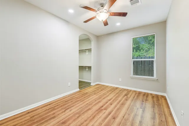 an empty room with wooden floor chandelier fan and windows