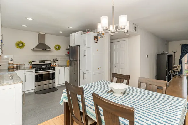 a kitchen with stainless steel appliances kitchen island granite countertop a refrigerator a stove a sink dishwasher and white cabinets with wooden floor