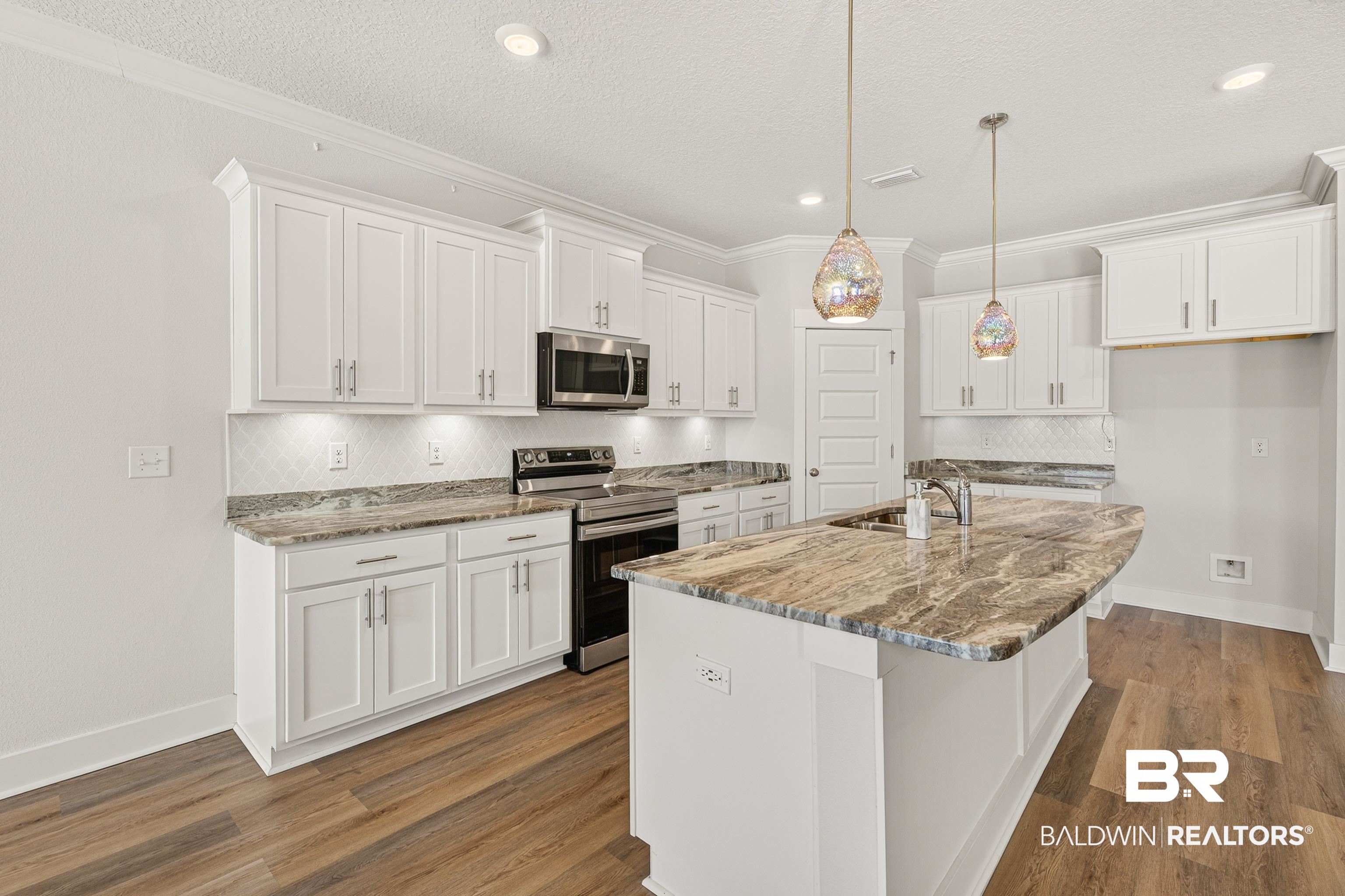 1724 Partridge Street Foley, AL 36535 - Photo 18 of 62 Kitchen featuring a large island with a natural stone countertop, white shaker-style cabinetry, stainless steel appliances, a tile backsplash, and wood-finish flooring