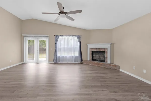 a view of an empty room with wooden floor fireplace and a window