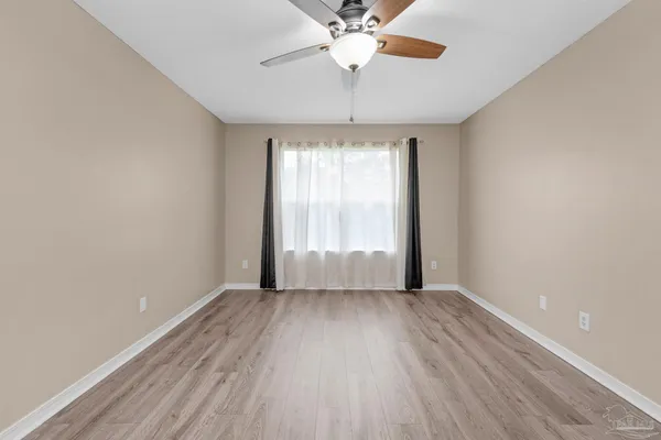 an empty room with wooden floor chandelier fan and windows