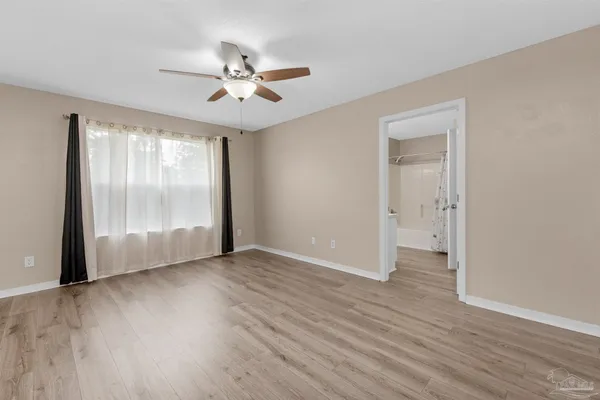 an empty room with wooden floor fan and windows