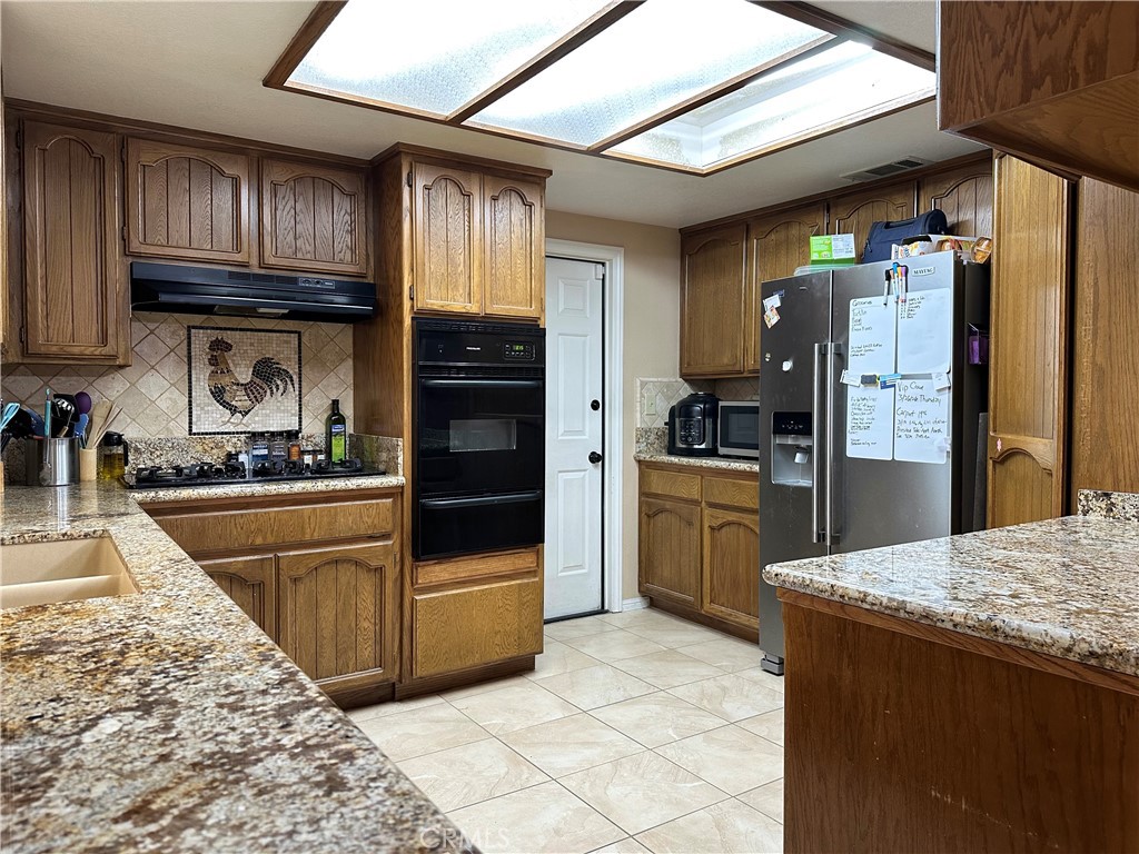 18143 Kalin Ranch Drive Victorville, CA 92395 - Photo 14 of 28 a kitchen with granite countertop a refrigerator and wooden cabinets