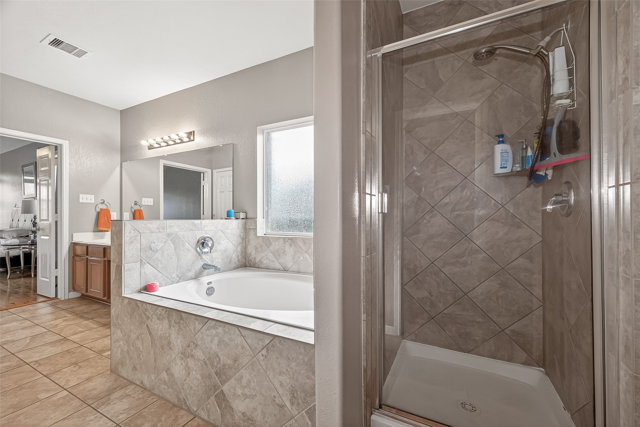 9110 Cavalier Lane Rosenberg, TX 77469 - Photo 26 of 30 This bathroom features a modern design with a tiled walk-in shower and a spacious bathtub. It has a large mirror, ample lighting, and a vanity with storage space.