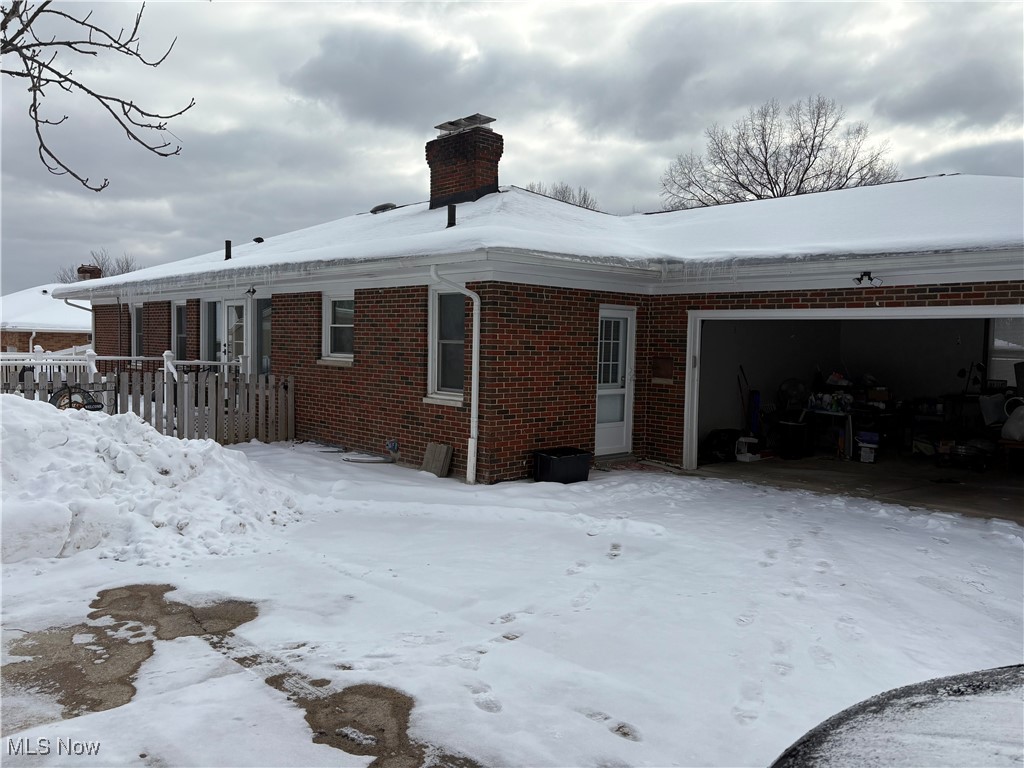 Snow covered back of property featuring a garage