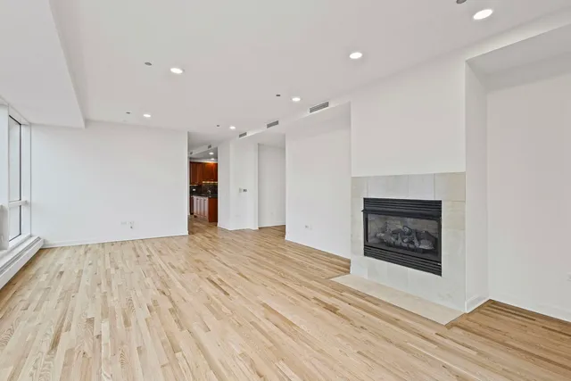 a view of an empty room with wooden floor a fireplace and a window