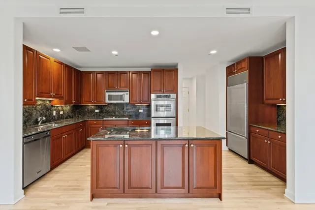 a kitchen with stainless steel appliances granite countertop wooden cabinets a refrigerator and a sink