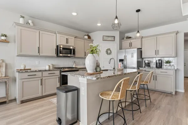 a kitchen with stainless steel appliances granite countertop a stove top oven a refrigerator a sink and white cabinets with wooden floor