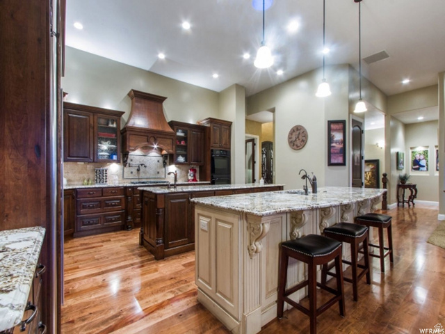 4378 Foothill Drive Bountiful, UT 84010 - Photo 7 of 46 Spacious kitchen featuring two islands with stone countertops, a decorative wood range hood, rich wood cabinetry, and wood-finish flooring