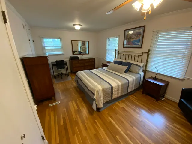 a bedroom with a bed a mirror on dresser and a wooden floor