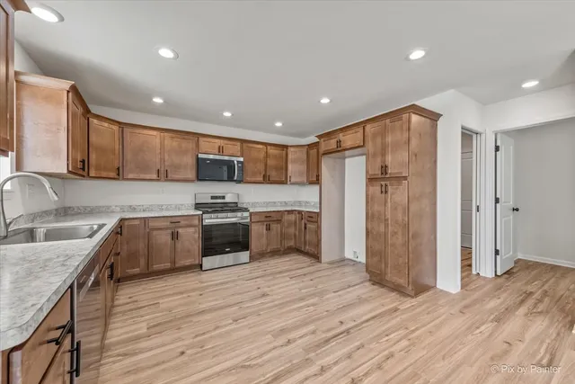 a kitchen with stainless steel appliances granite countertop a refrigerator a sink dishwasher a stove and a microwave oven with wooden floor