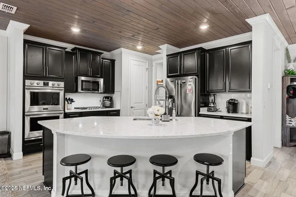 a kitchen with stainless steel appliances granite countertop a refrigerator a stove a sink a oven with white cabinets and chairs