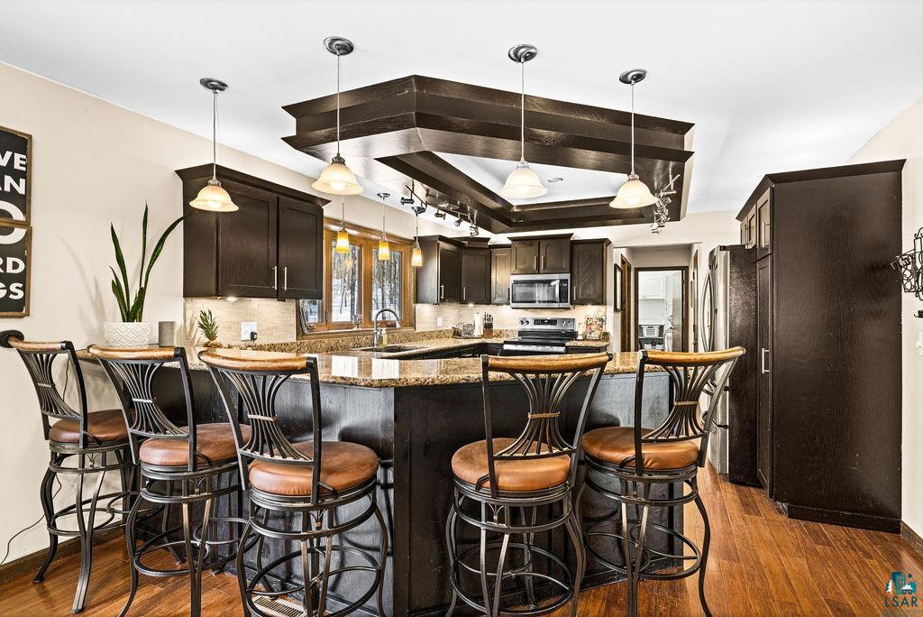 421 St Louis River Road Proctor, MN 55810 - Photo 24 of 57 Kitchen with dark wood finish cabinetry, a peninsula, a kitchen bar, stainless steel appliances, and a raised ceiling