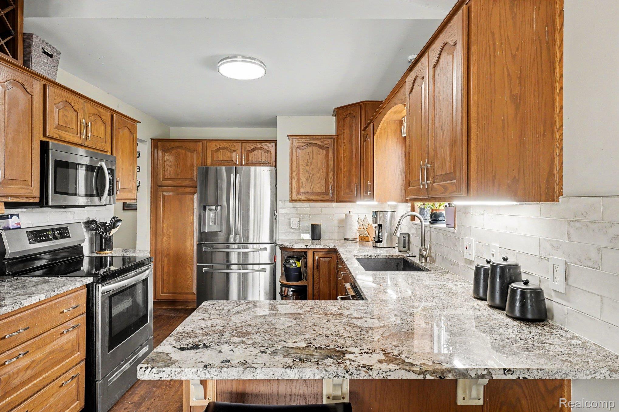4848 Columbiaville Road Columbiaville, MI 48421 - Photo 5 of 35 Kitchen featuring wood cabinetry, granite countertops, stainless steel appliances, a tile backsplash, and wood-finish flooring