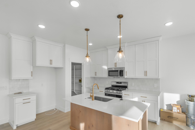 537 South Rivergate Drive Logan, UT 84321 - Photo 4 of 20 Contemporary kitchen featuring a central island with an undermount sink, white shaker cabinetry, stainless steel appliances, recessed ceiling lights, and wood-finish flooring