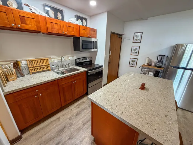 a kitchen with stainless steel appliances granite countertop a sink a stove top oven a chimney and wooden floor