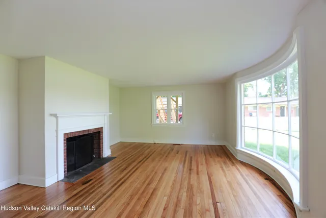 an empty room with wooden floor fireplace and windows