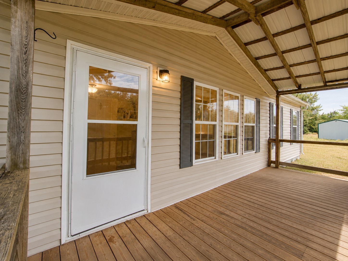 461924 East 1140 Road Sallisaw, OK 74955 - Photo 5 of 29 Covered porch with wood-finish flooring, white storm door, multiple windows with dark shutters, and beige siding