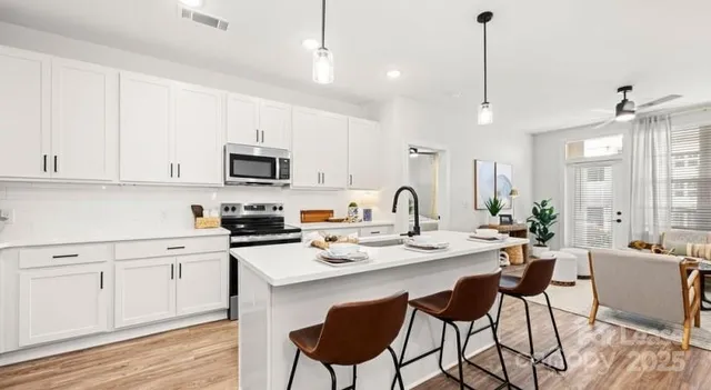 a kitchen with stainless steel appliances a stove a sink a microwave a refrigerator and white cabinets with wooden floor