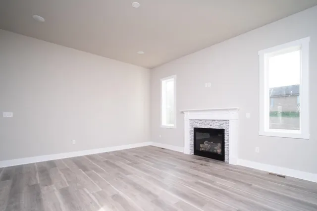 a view of an empty room with wooden floor fireplace and a window