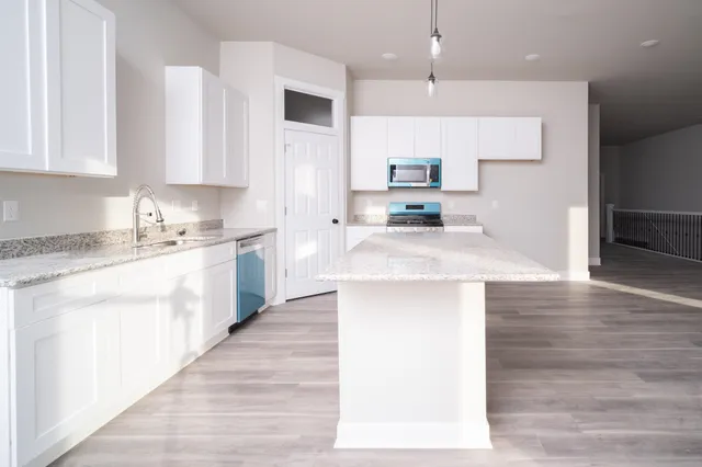 a kitchen with stainless steel appliances kitchen island granite countertop a sink a stove and white cabinets with wooden floor