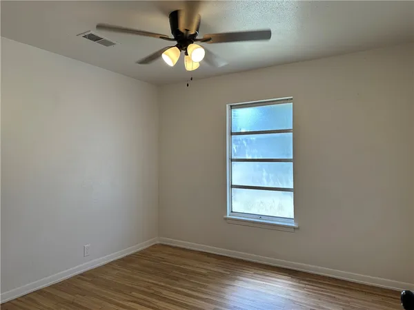 an empty room with wooden floor fan and windows