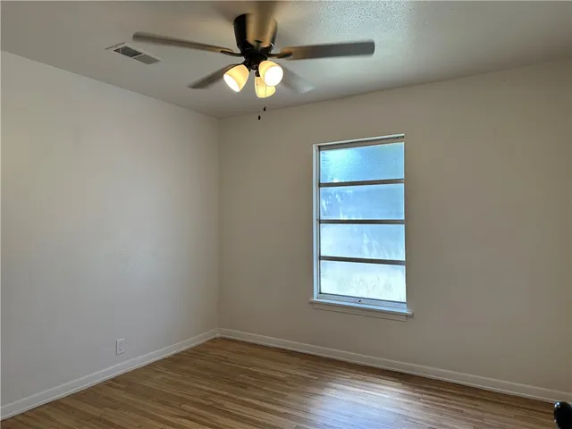 an empty room with wooden floor fan and windows