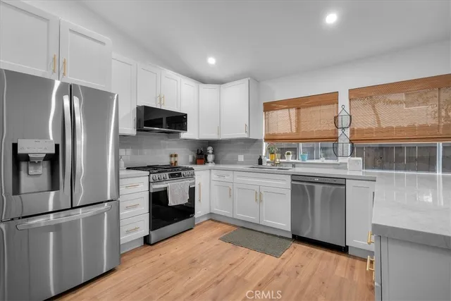 a kitchen with stainless steel appliances granite countertop a stove a sink dishwasher a refrigerator and a microwave oven with wooden floor