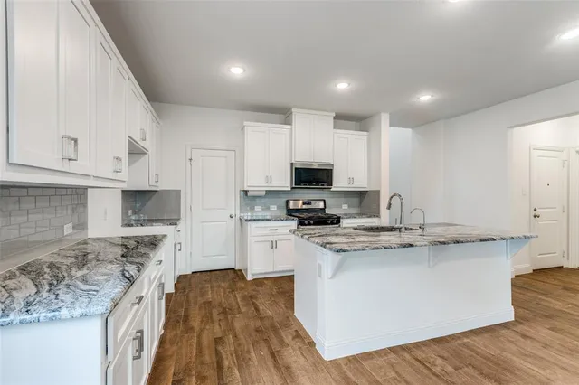 a kitchen with stainless steel appliances granite countertop a stove a sink and white cabinets