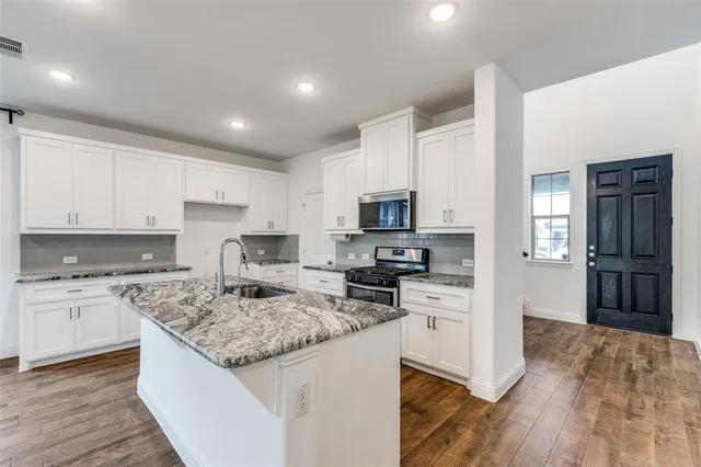 a kitchen with stainless steel appliances granite countertop a stove top oven a refrigerator a sink and dishwasher with wooden floor