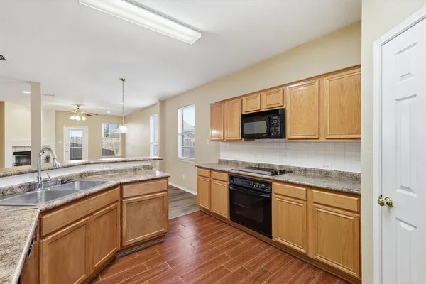 a kitchen with stainless steel appliances granite countertop a stove top oven a sink dishwasher and a refrigerator with wooden floor